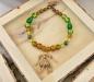 Preview: Keltische Glasperlenkette in grün und gold - Fibelkette mit Klapperanhänger aus Bronze von Belanas Schatzkiste auf einem Holztabeltt